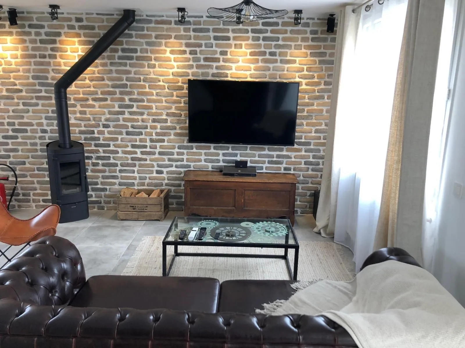 Salon avec mur en briques, poêle noir et canapé Chesterfield