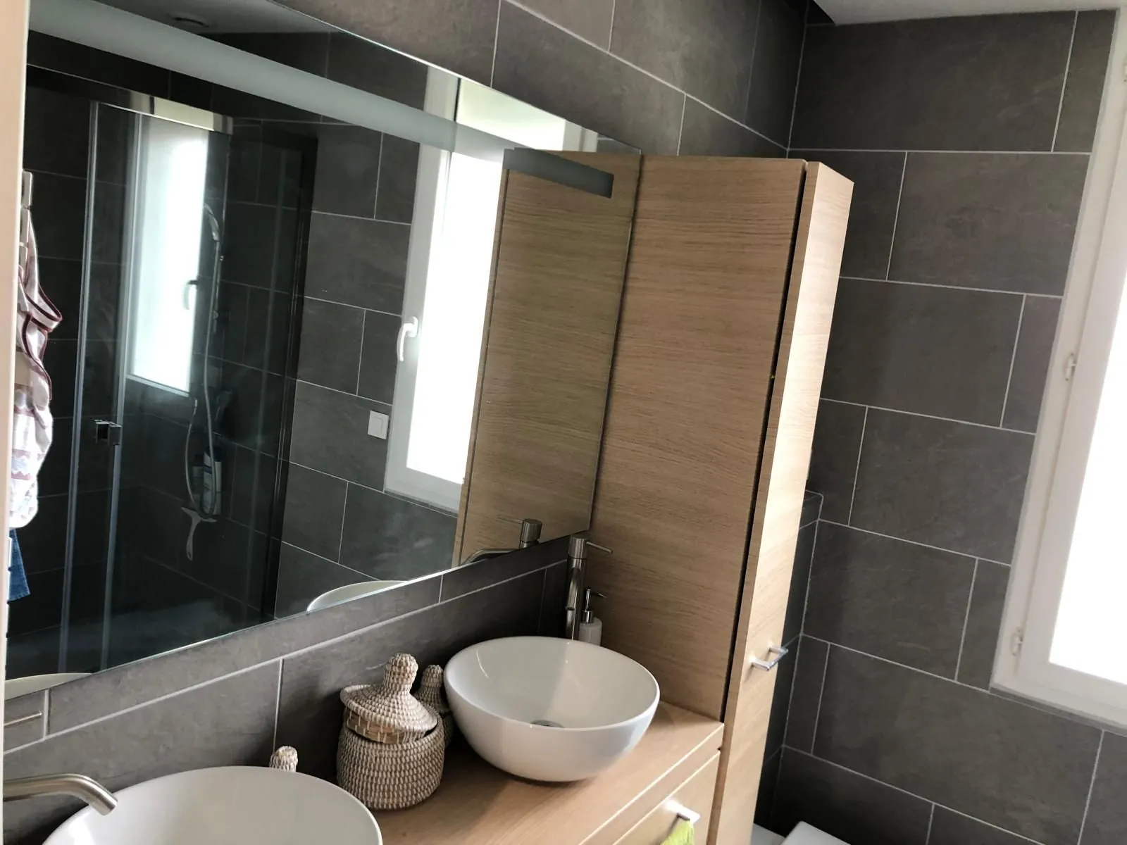 Salle de bain avec carrelage gris foncé, vasque et meuble en bois clair