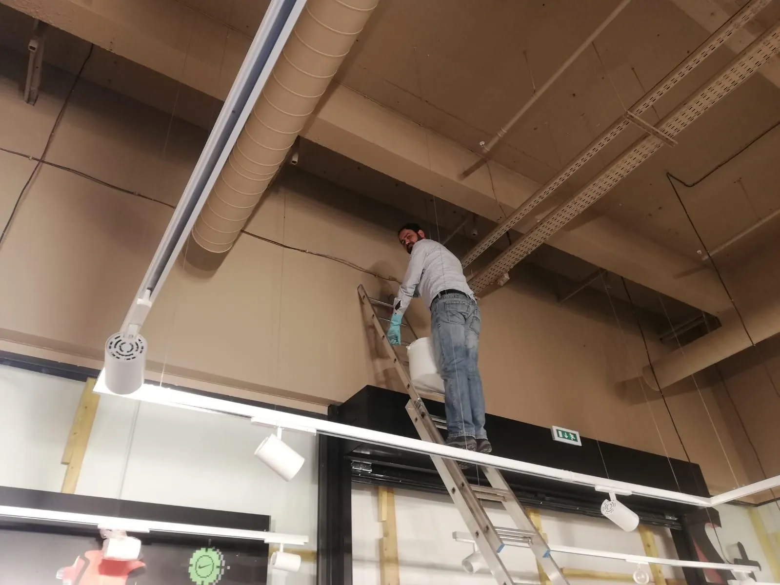 Ouvrier sur une échelle installant des rails d'éclairage au plafond